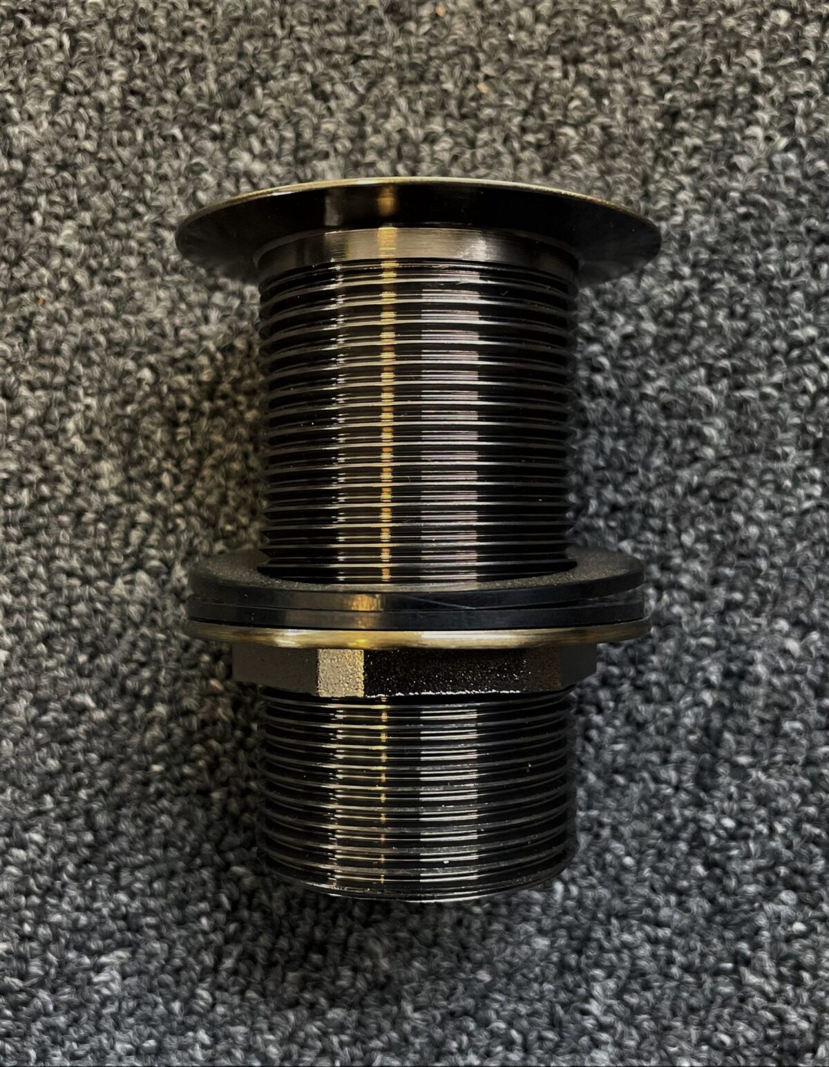 Bronze pop-up waste fitting on textured surface.