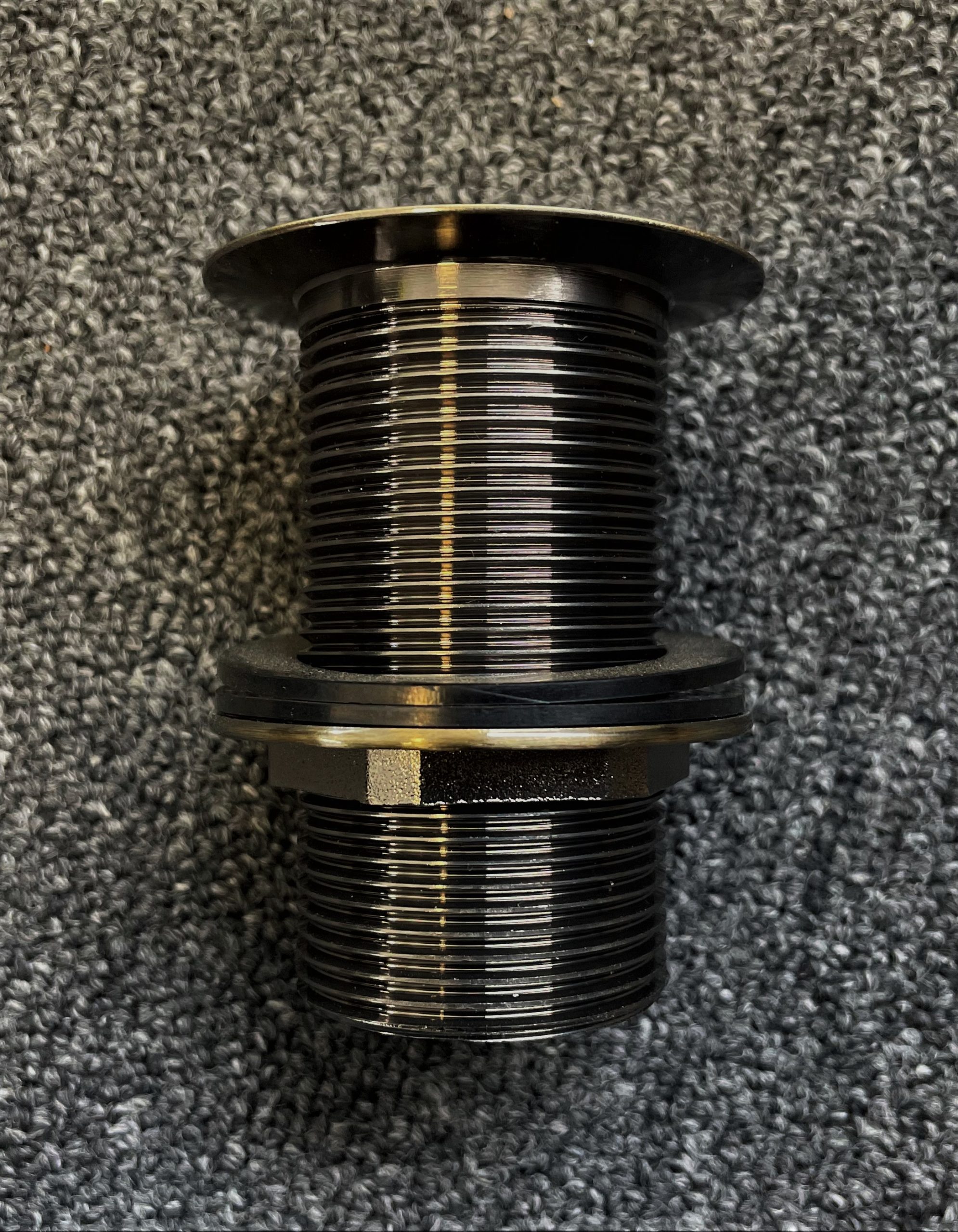 Bronze pop-up waste fitting on textured surface.