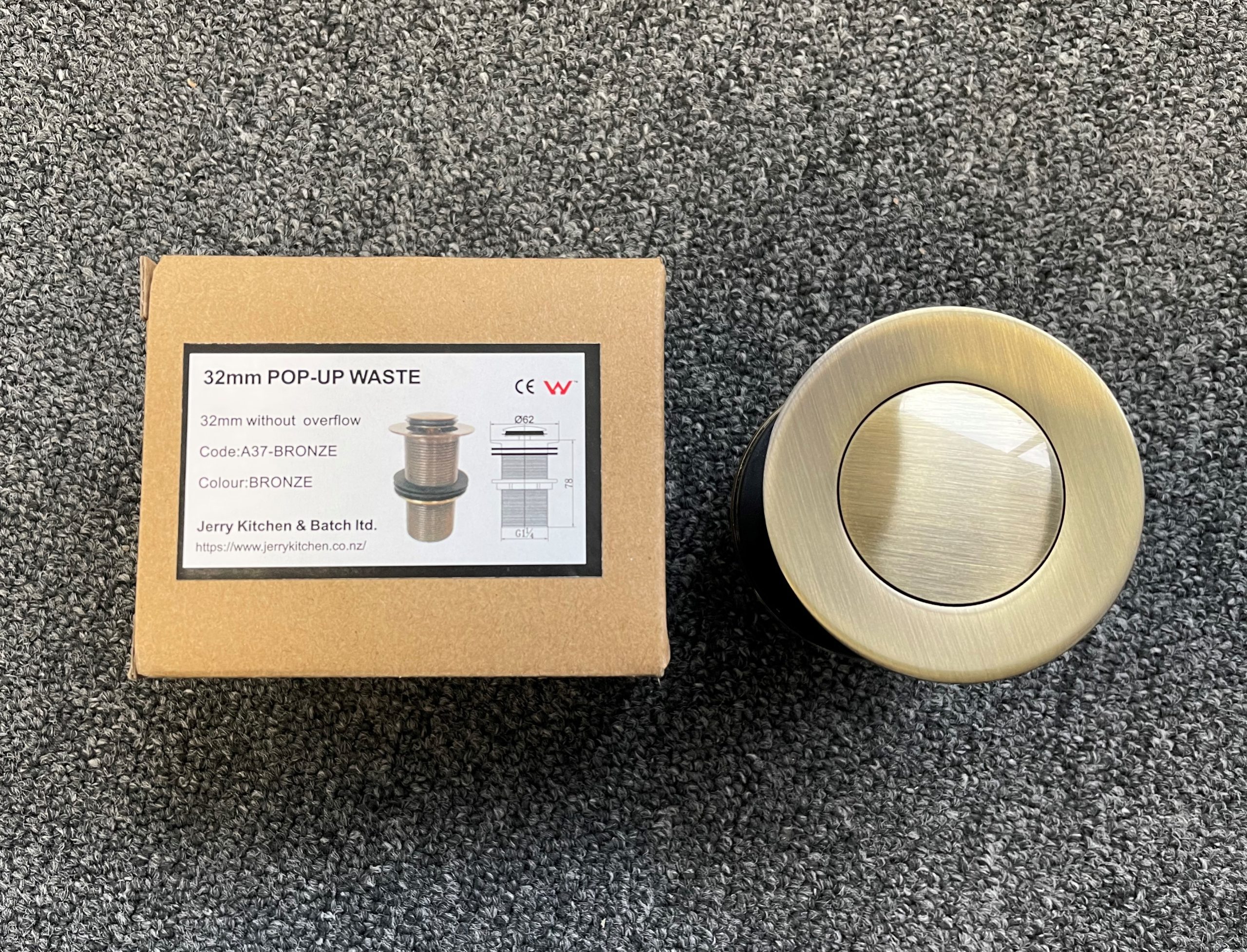 Bronze 32mm pop-up waste with packaging on carpet.