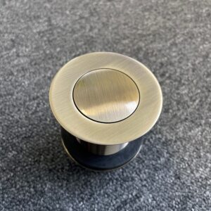 Bronze pop-up waste plug on gray surface, top view.