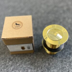 Gold pop-up waste drain with packaging on gray surface.