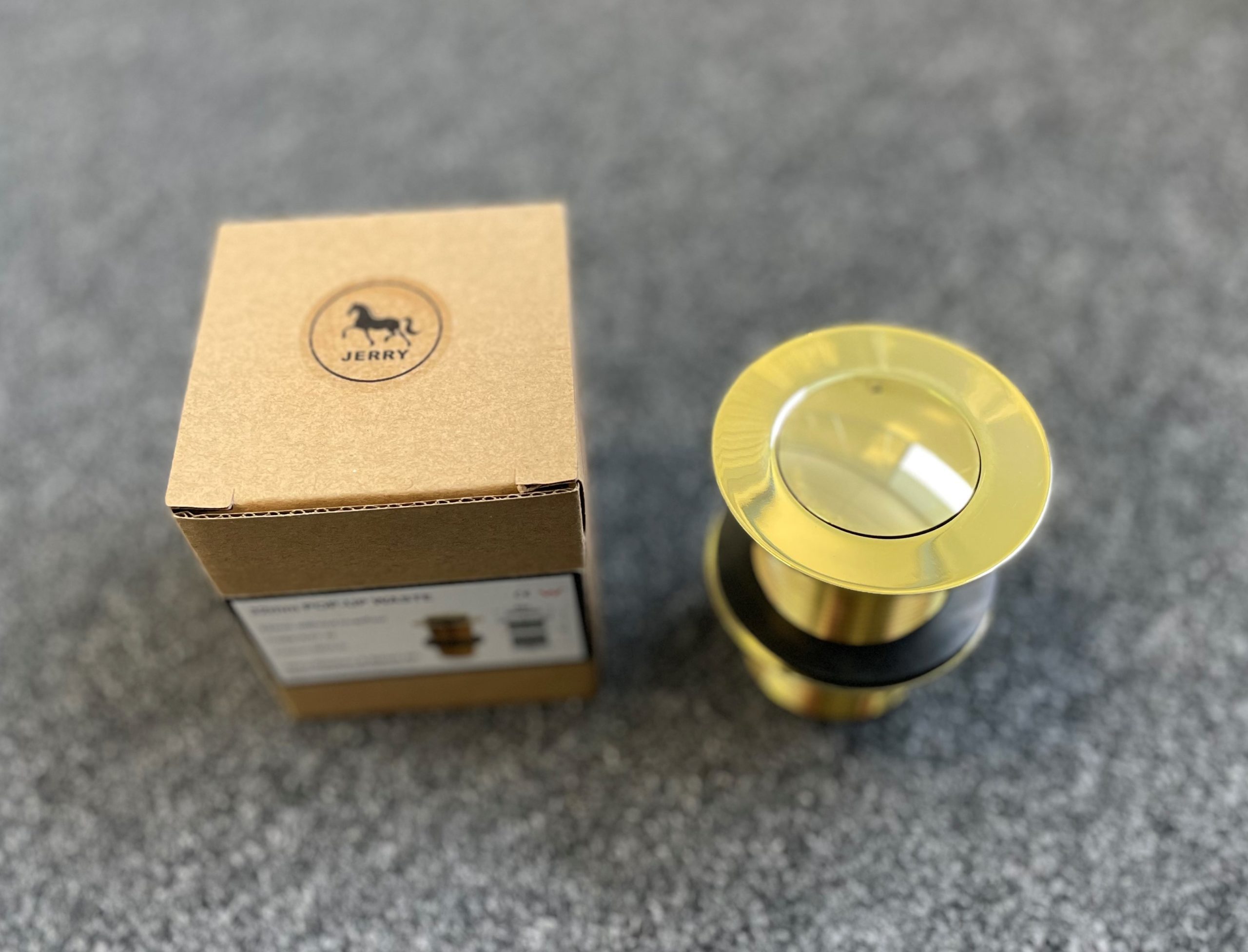 Gold pop-up waste drain with packaging on gray surface.