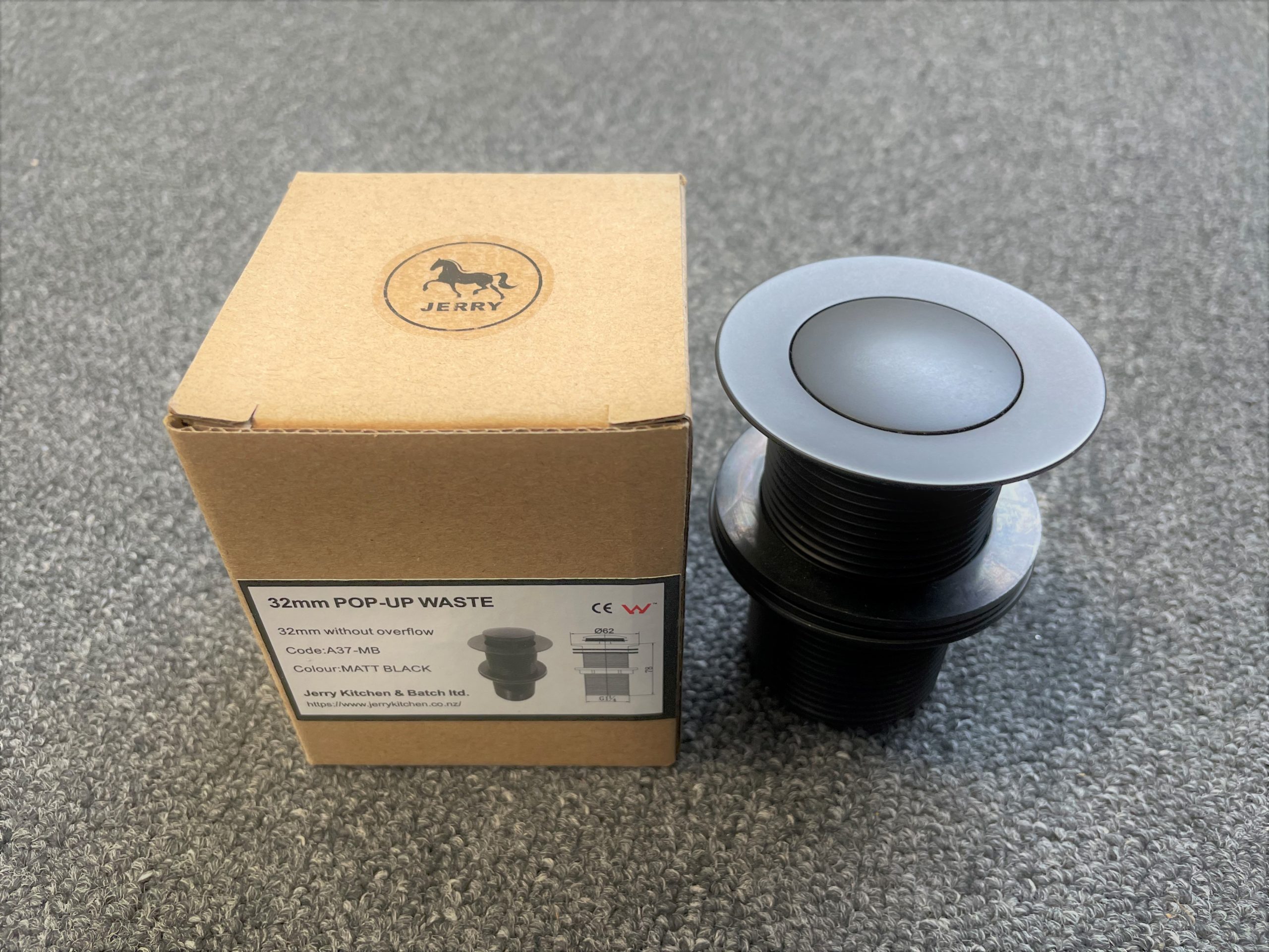 32mm pop-up waste in matte black with packaging on a gray surface.