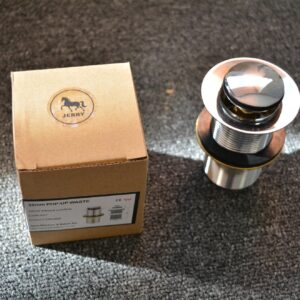 Chrome pop-up waste without overflow next to a cardboard box on carpet.