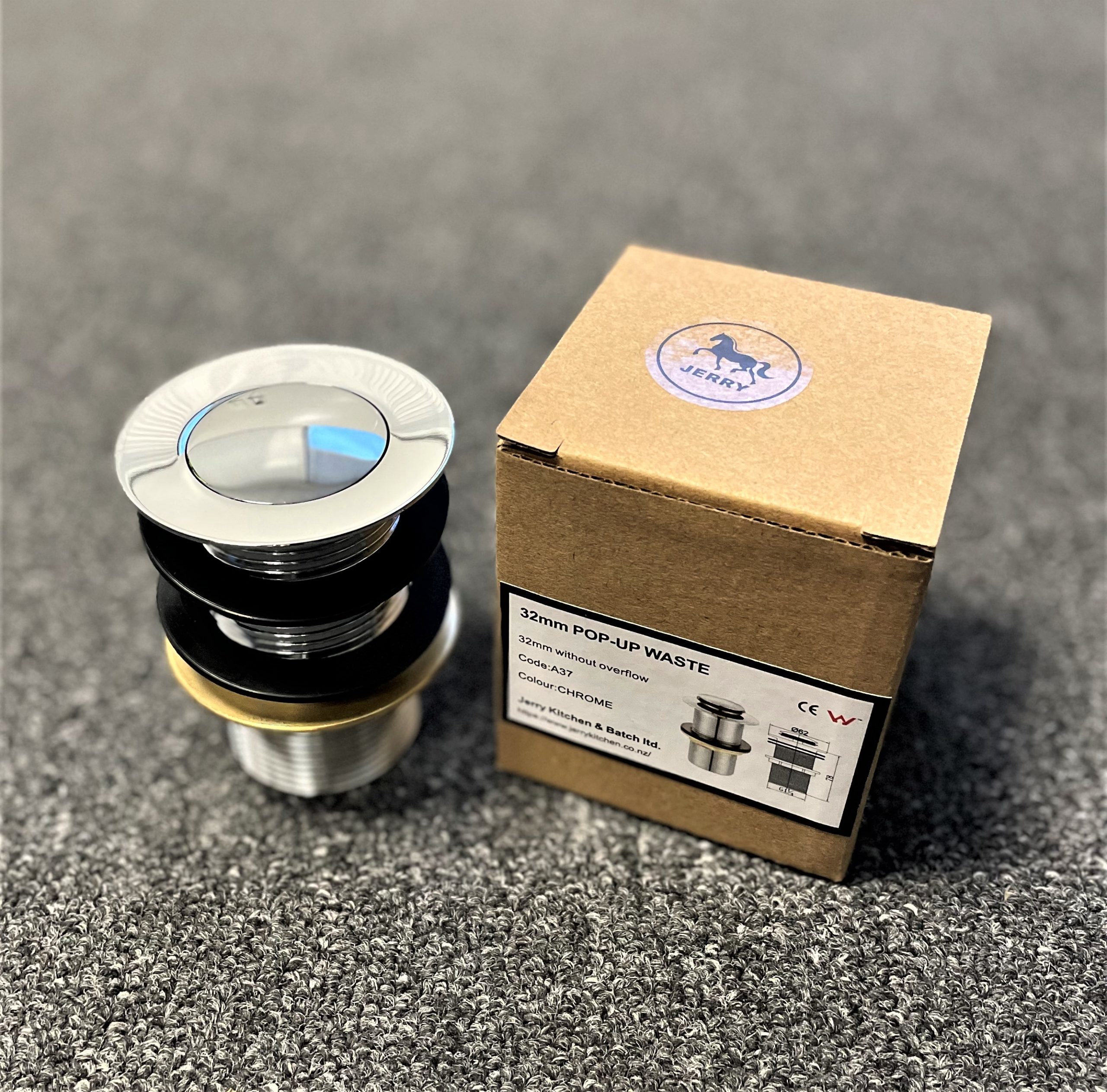 Chrome pop-up waste without overflow next to packaging on carpeted surface.