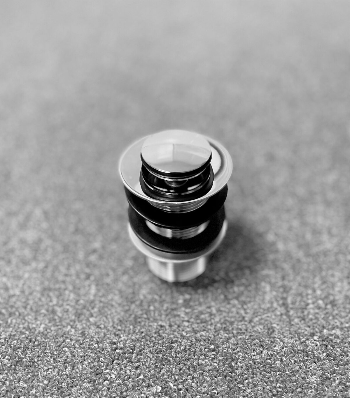 Chrome pop-up waste without overflow on textured surface.