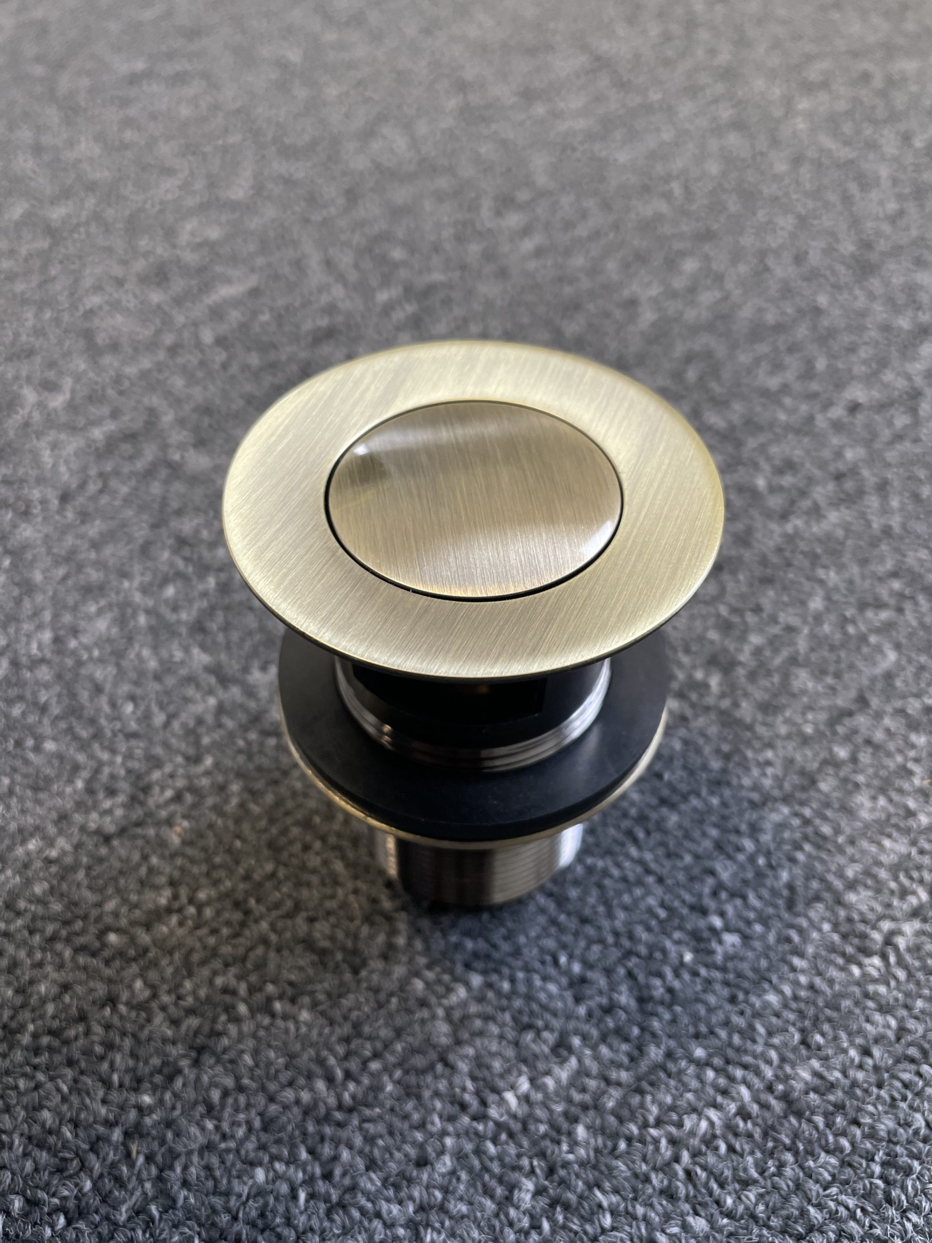 Bronze pop-up waste with overflow on textured surface.