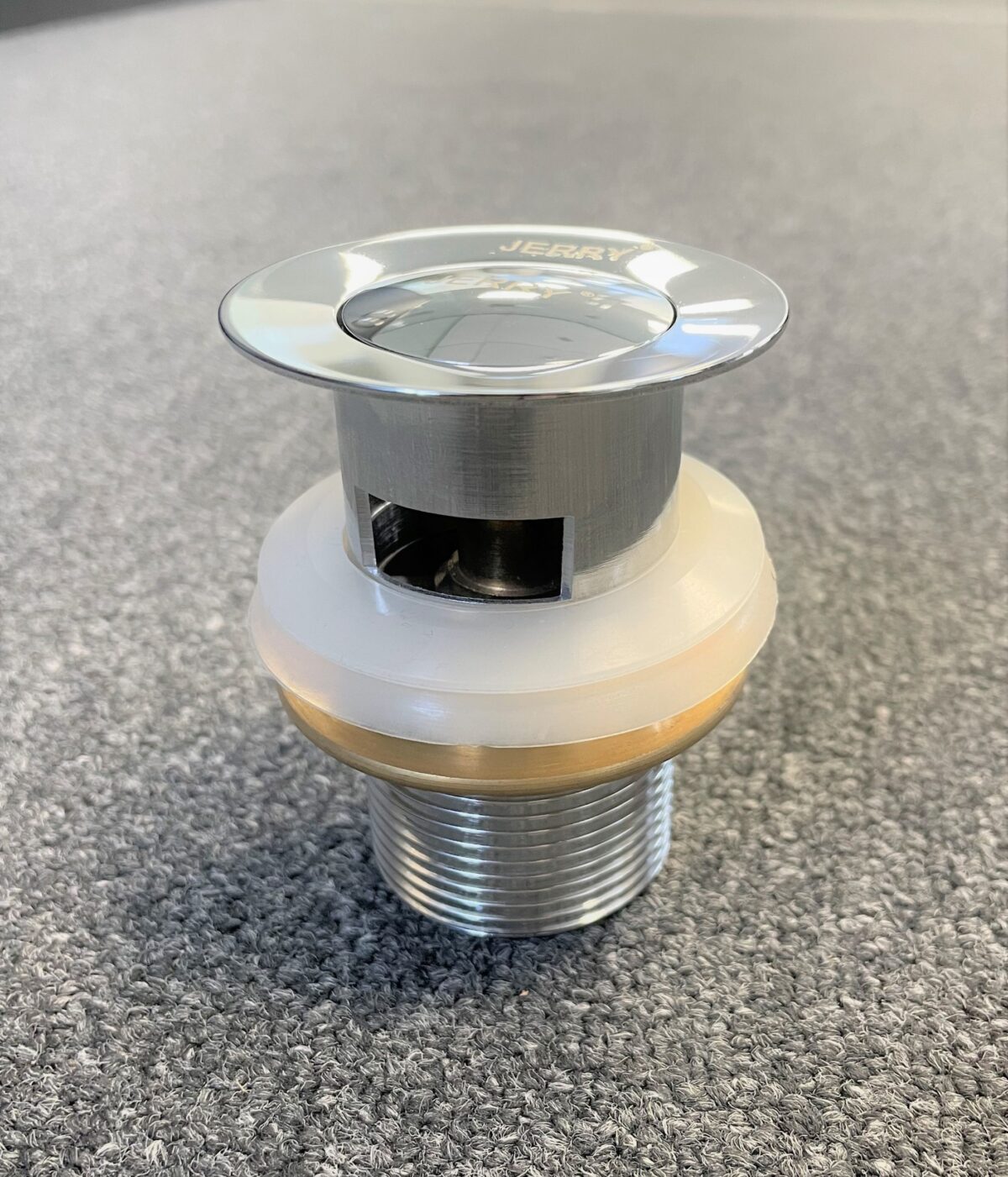 Chrome solid brass pop-up waste with overflow on gray surface.