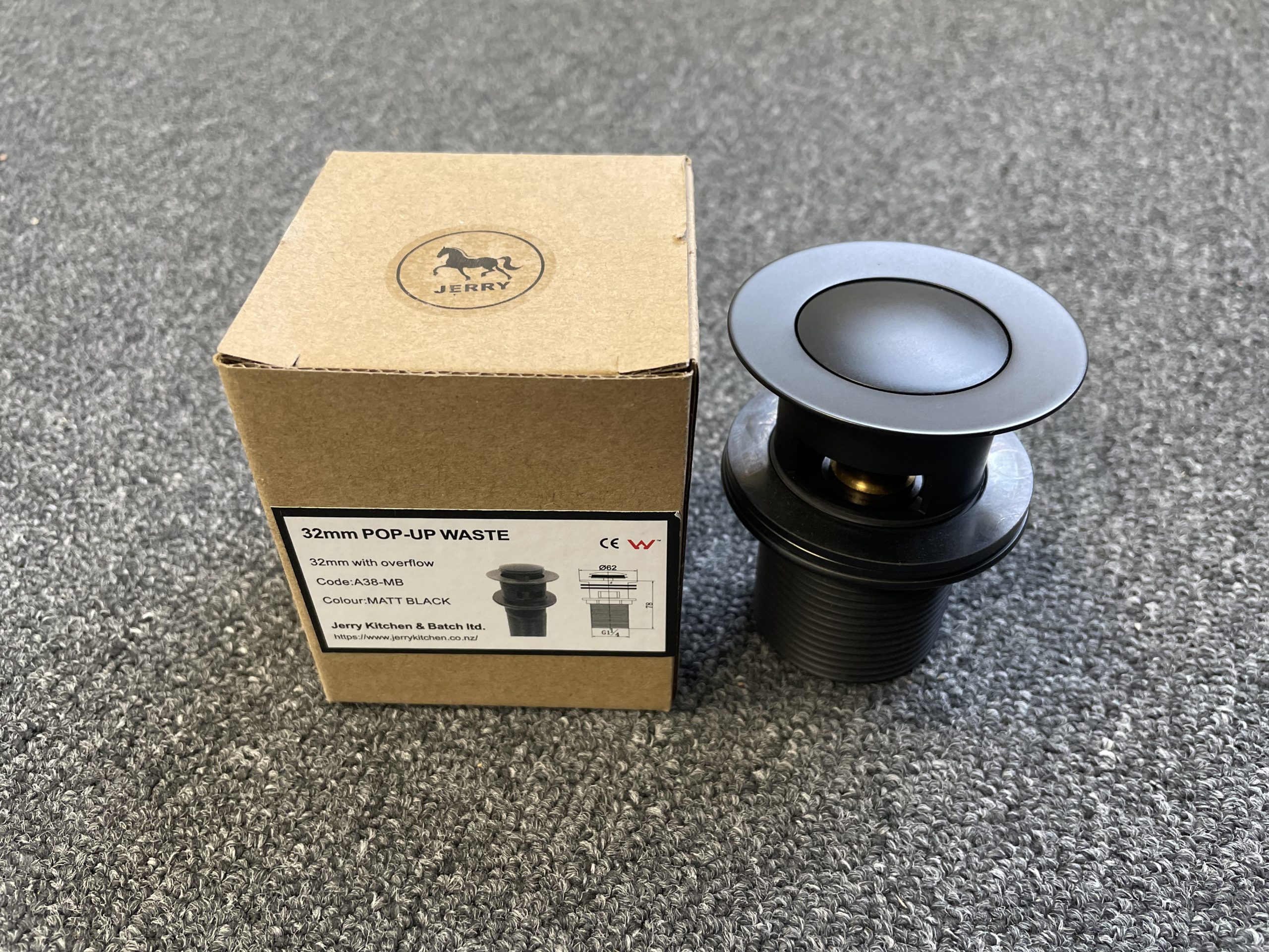 Matt black pop-up waste with overflow next to packaging box.