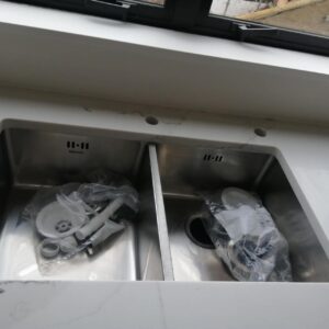 Double kitchen sink with plumbing parts on a marble countertop.