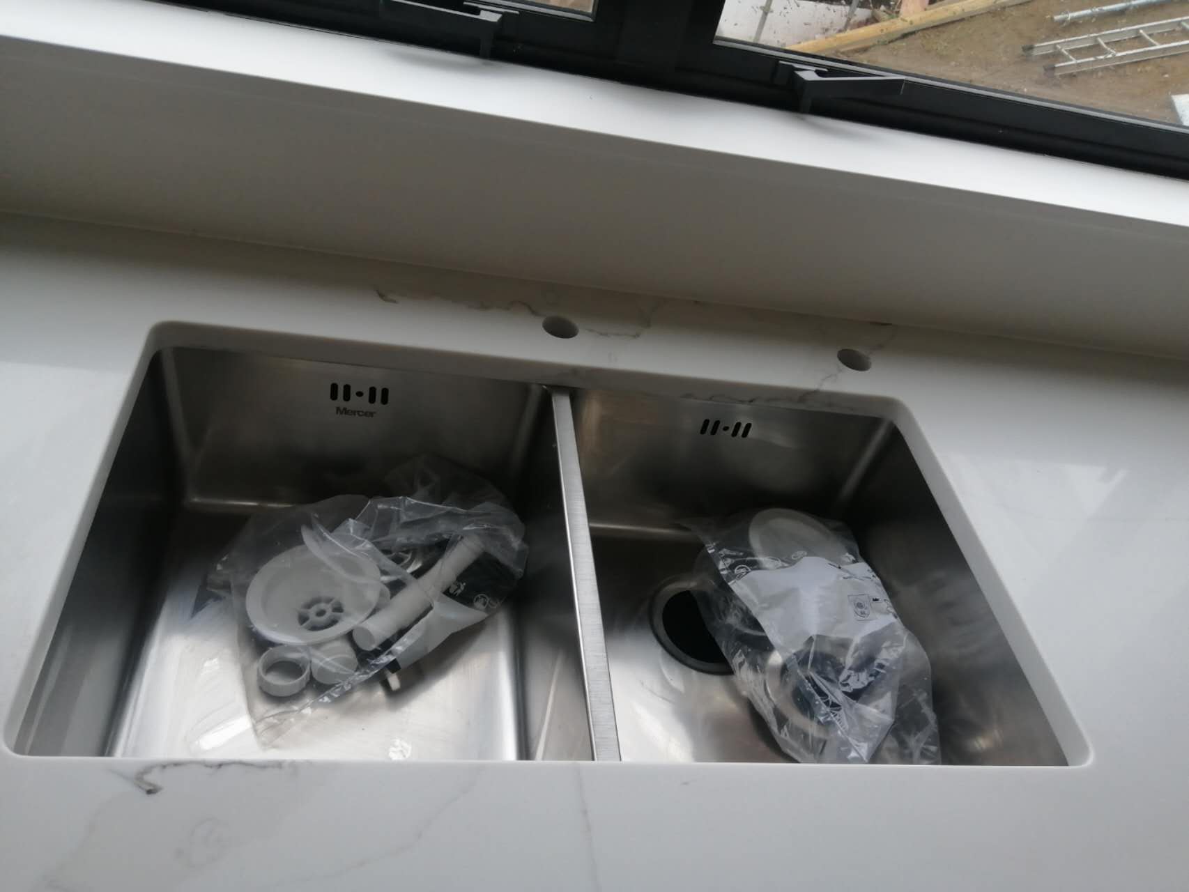 Double kitchen sink with plumbing parts on a marble countertop.