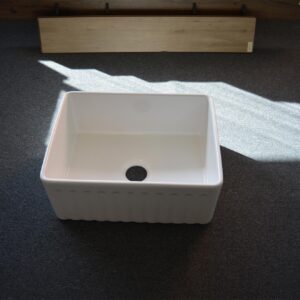 White ceramic kitchen sink on dark carpeted floor.