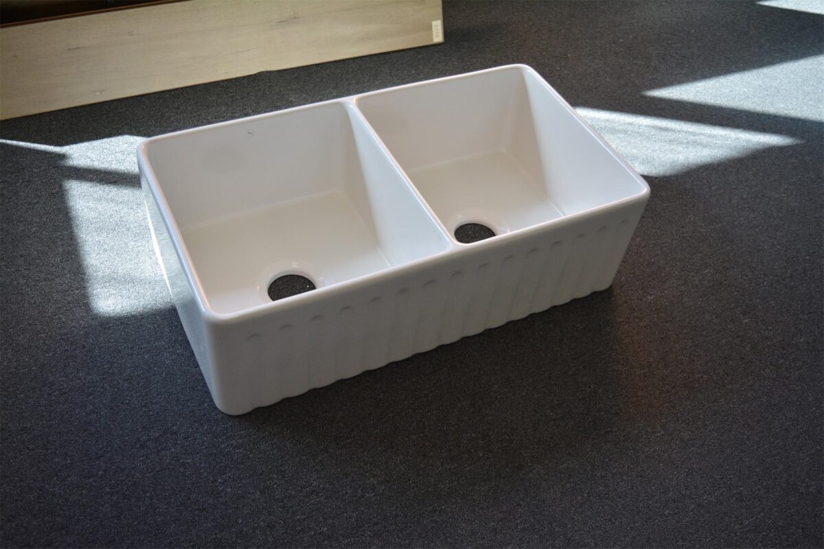 Double bowl white kitchen sink on dark carpet.