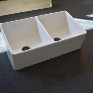 Double bowl white kitchen sink on dark carpet.