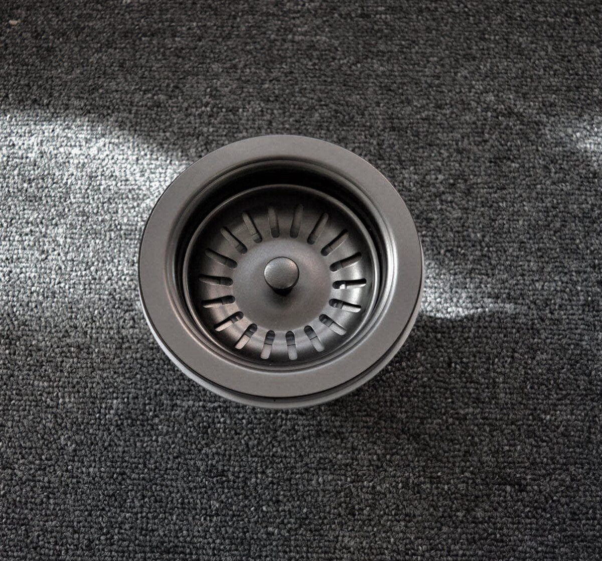 A stainless steel sink strainer on a dark carpet.