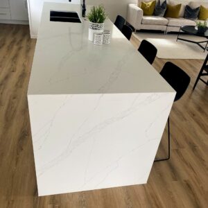 Modern kitchen island with white marble countertop and black chairs.