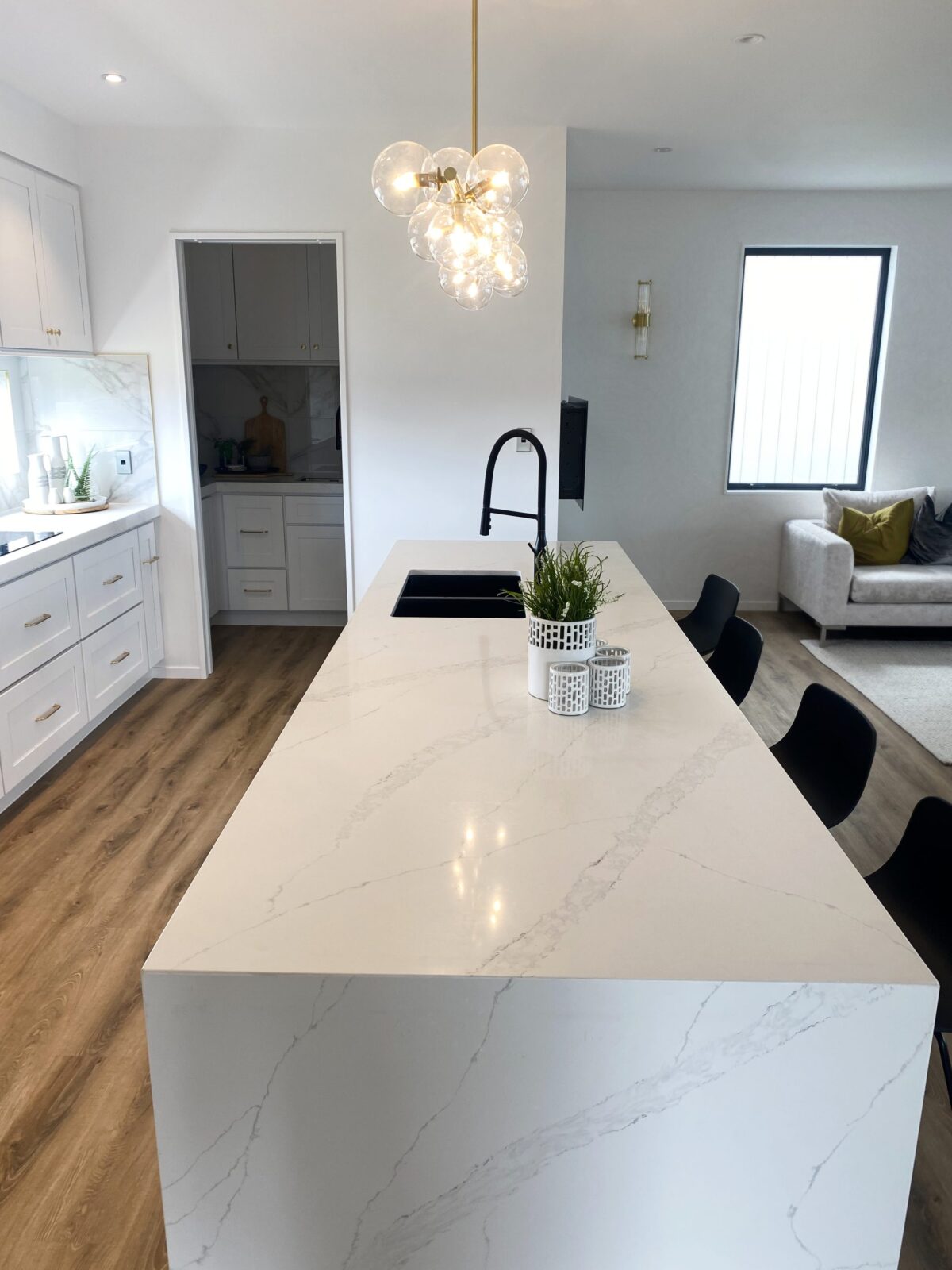 Modern kitchen with marble island, pendant light, and black chairs.