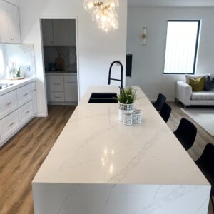 Modern kitchen with marble island, pendant light, and black chairs.