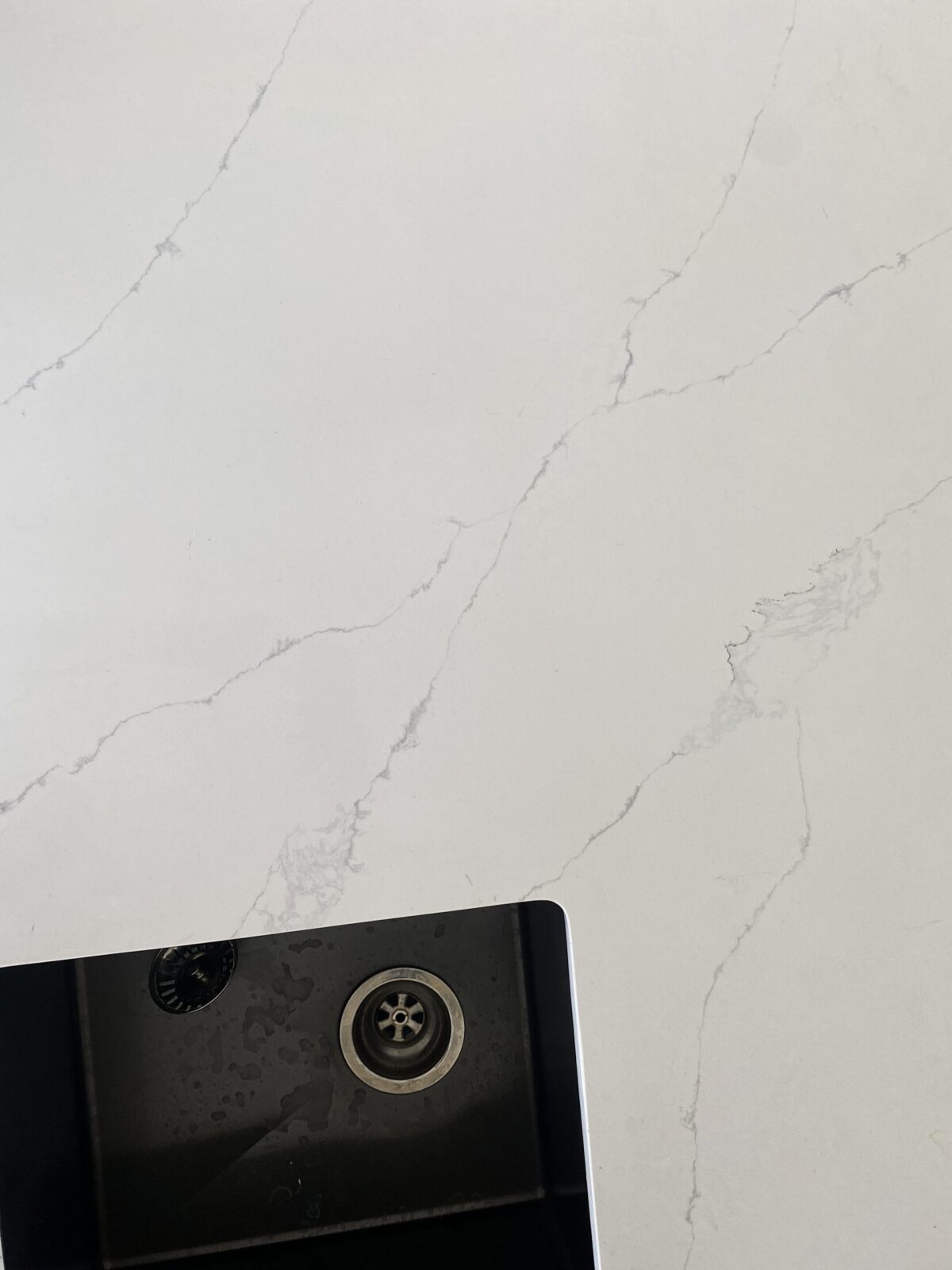 White marble countertop with subtle gray veining and a black sink corner.