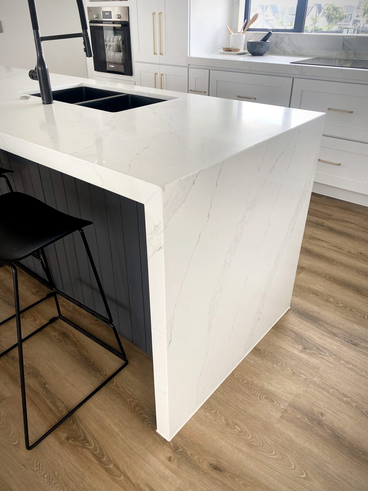 Modern kitchen with white marble countertop and black stool.
