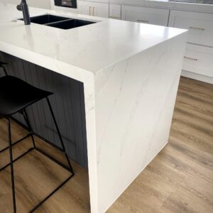 Modern kitchen with white marble countertop and black stool.