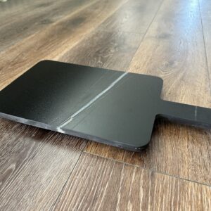 Black cutting board on wooden floor.
