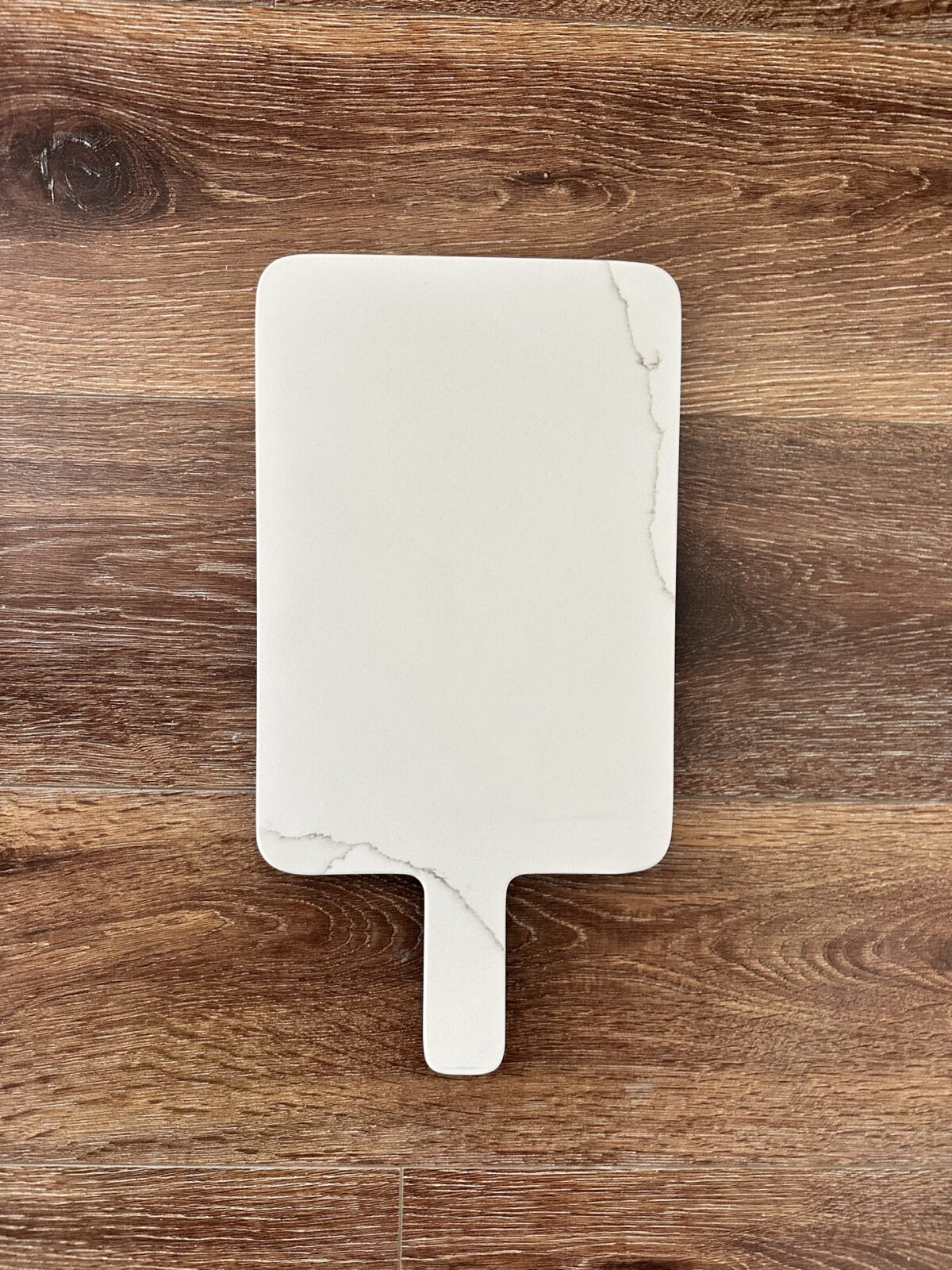 White marble cutting board on wooden surface.