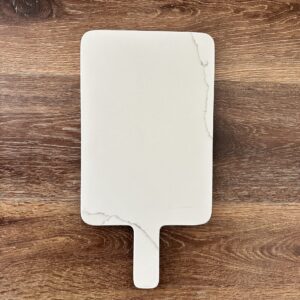 White marble cutting board on wooden surface.