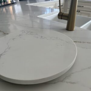 Marble kitchen countertop with round cutting board and gold faucet.