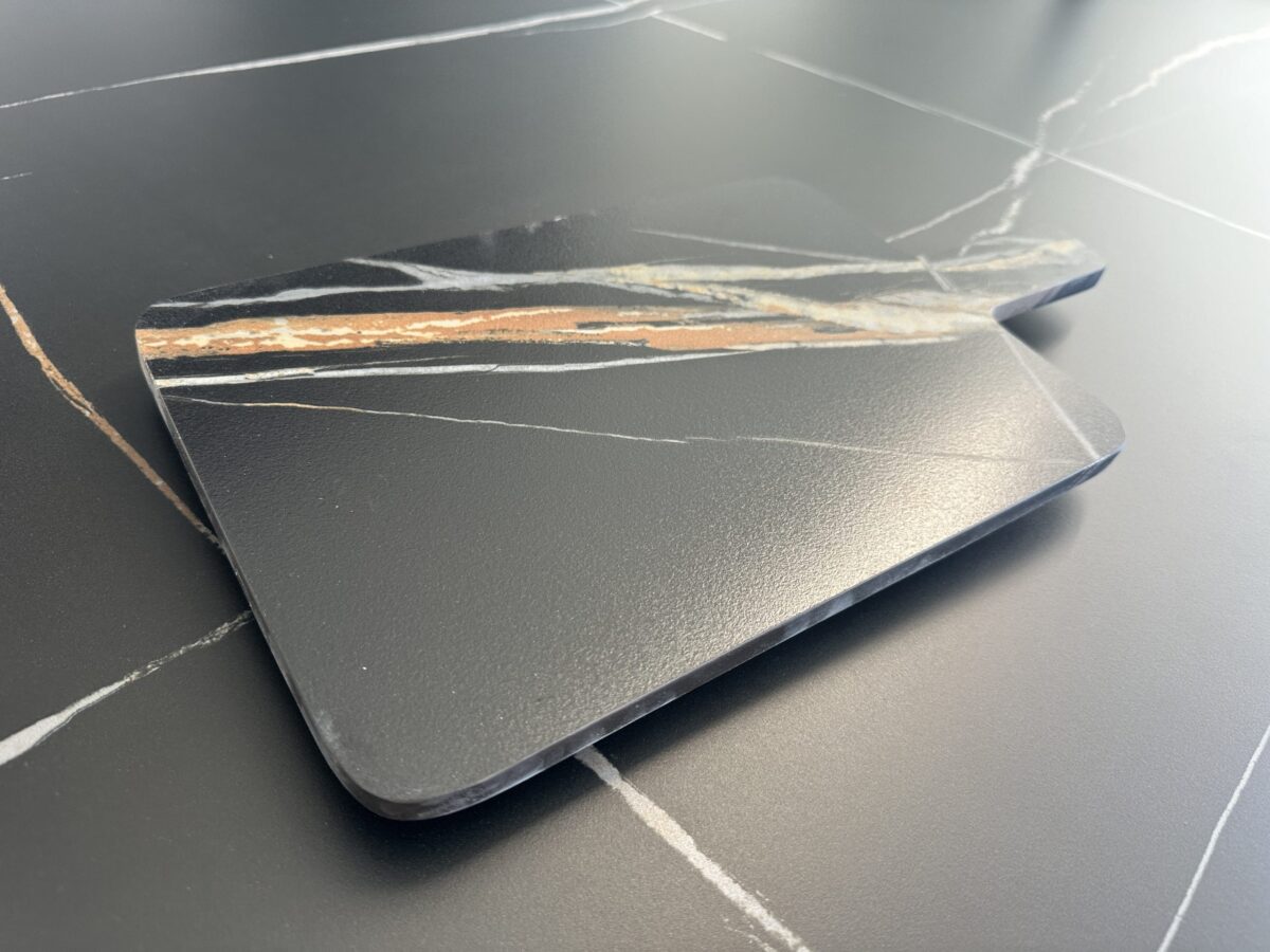 Black marble cutting board with white and brown veining on a matching surface.