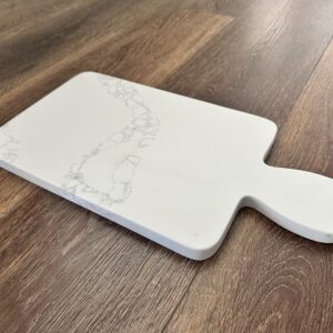 White marble cutting board on wooden floor.