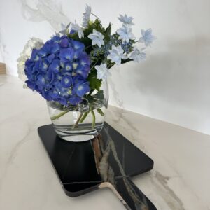 Blue and white flowers in a glass vase on a marble surface.