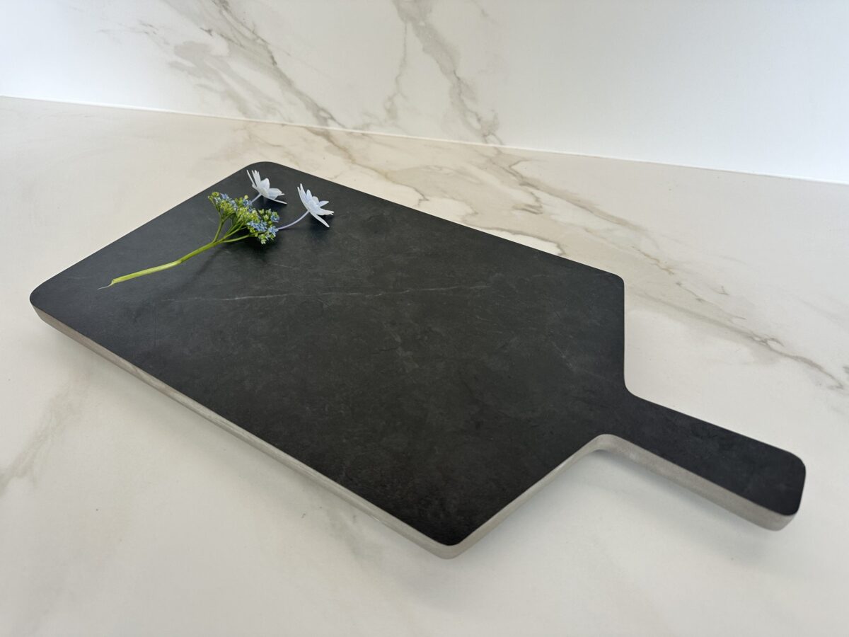 Black cutting board with flowers on marble countertop.