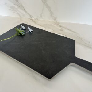 Black cutting board with flowers on marble countertop.