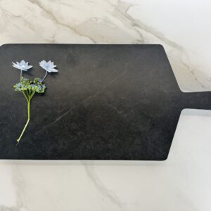 Black cutting board with two white flowers on a marble surface.