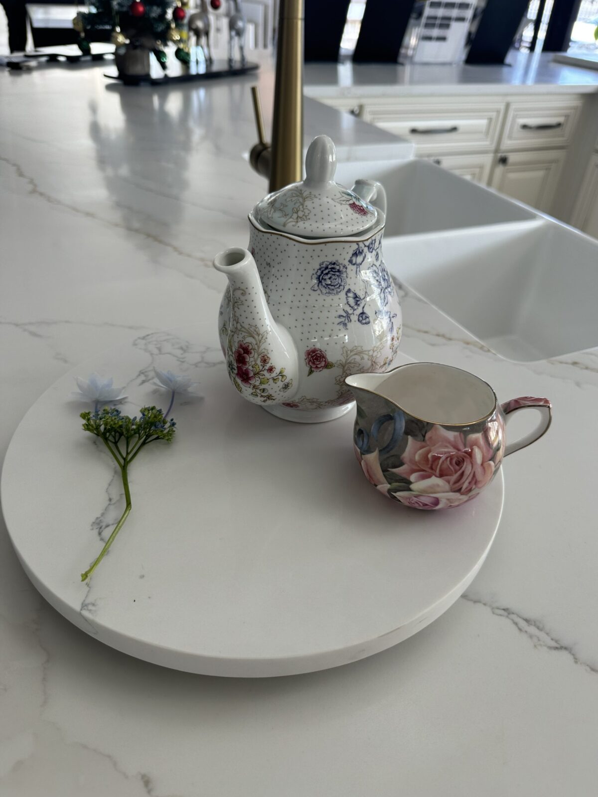 Floral teapot and creamer on marble counter with small flower.