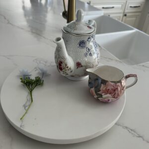 Floral teapot and creamer on marble counter with small flower.