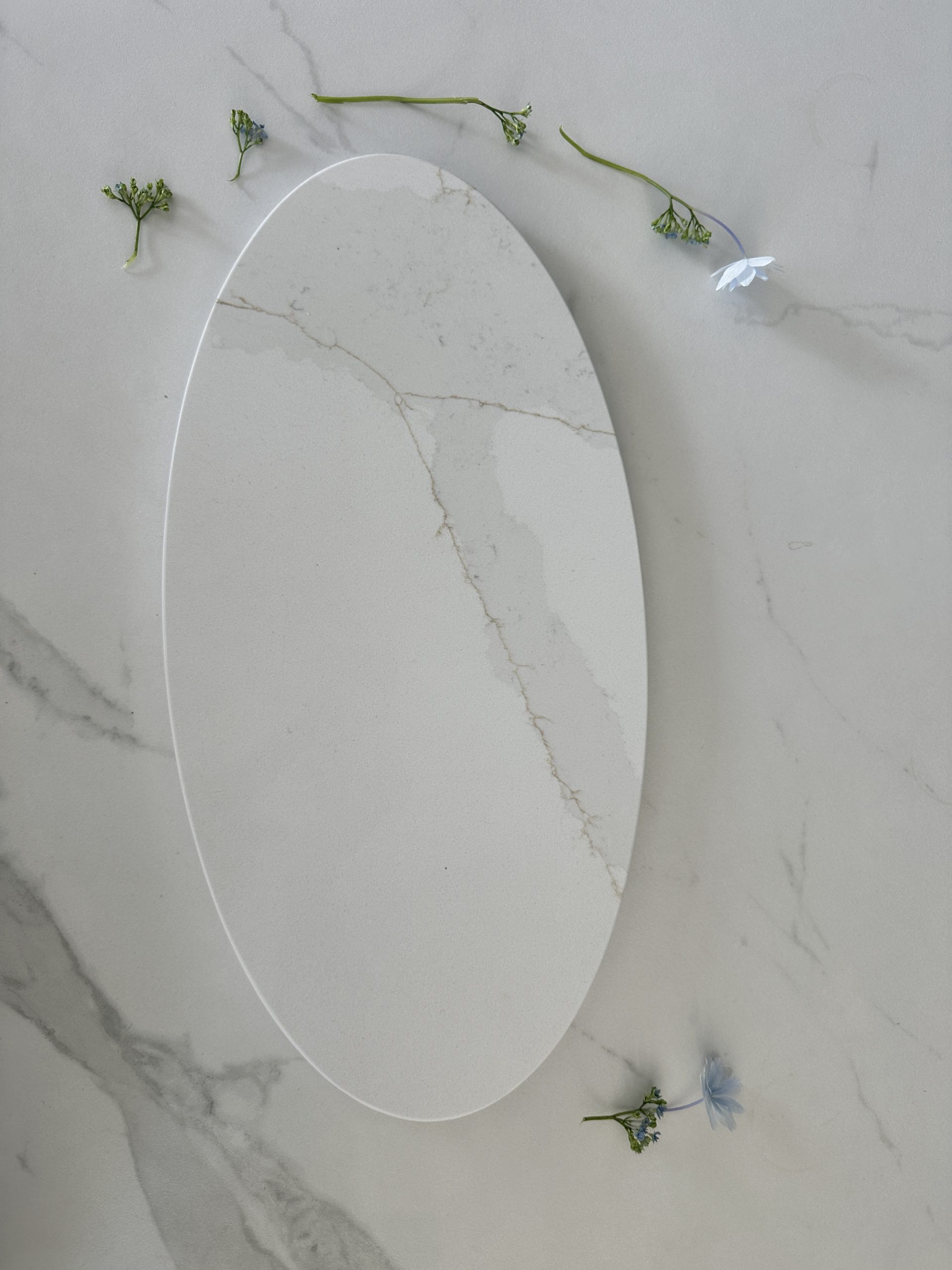 Oval marble platter on marble surface with scattered small flowers.