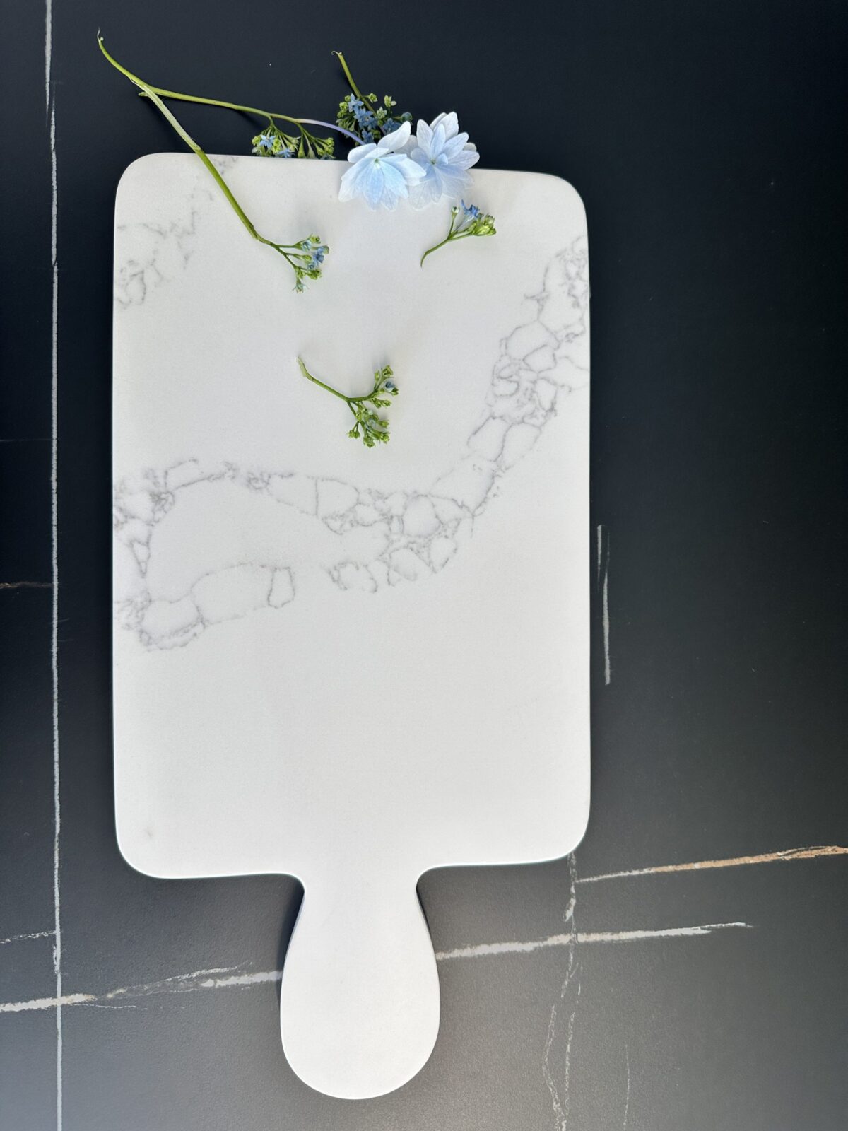 Marble cutting board with blue flowers on a dark surface.