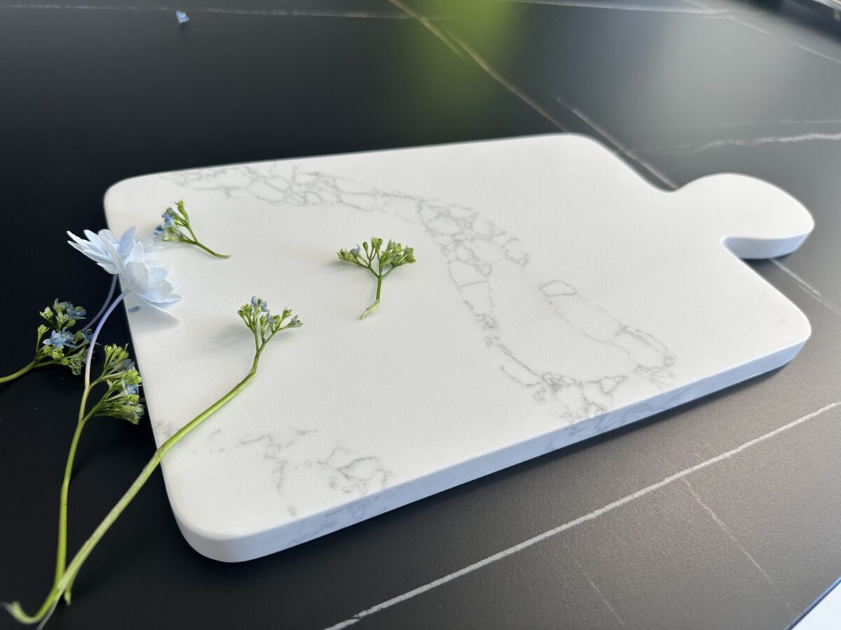 Marble cutting board with small flowers on a dark surface.