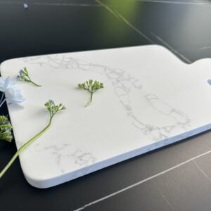 Marble cutting board with small flowers on a dark surface.