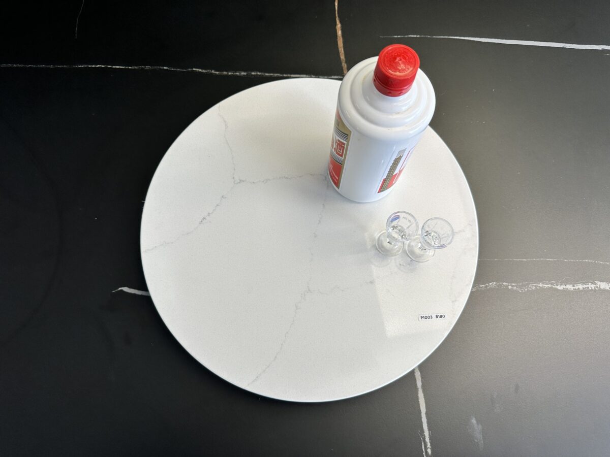 Marble lazy Susan with a bottle and small cups on a black surface.
