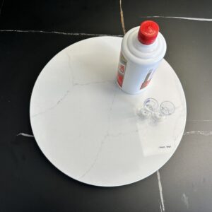 Marble lazy Susan with a bottle and small cups on a black surface.