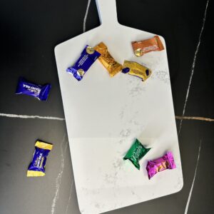 Marble cutting board with assorted wrapped chocolates on a dark surface.