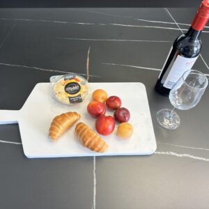 Cheese, croissants, plums, and wine on a marble cutting board.
