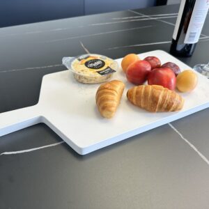 Cheese, croissants, and fruit on a cutting board with wine and glass nearby.