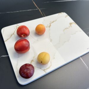 Five assorted fruits on a marble cutting board.