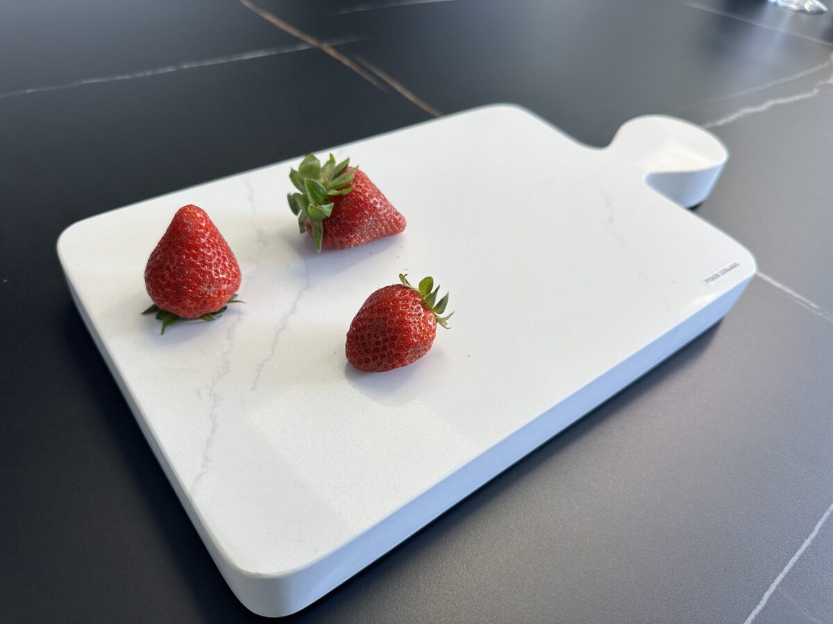 Three strawberries on a white cutting board.