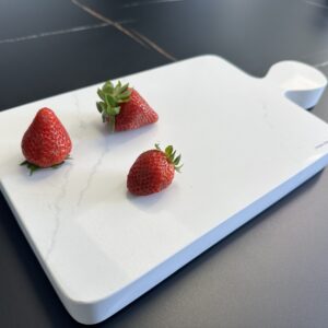 Three strawberries on a white cutting board.