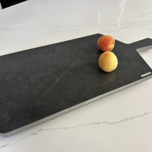 Cutting board with two peaches on a marble countertop.